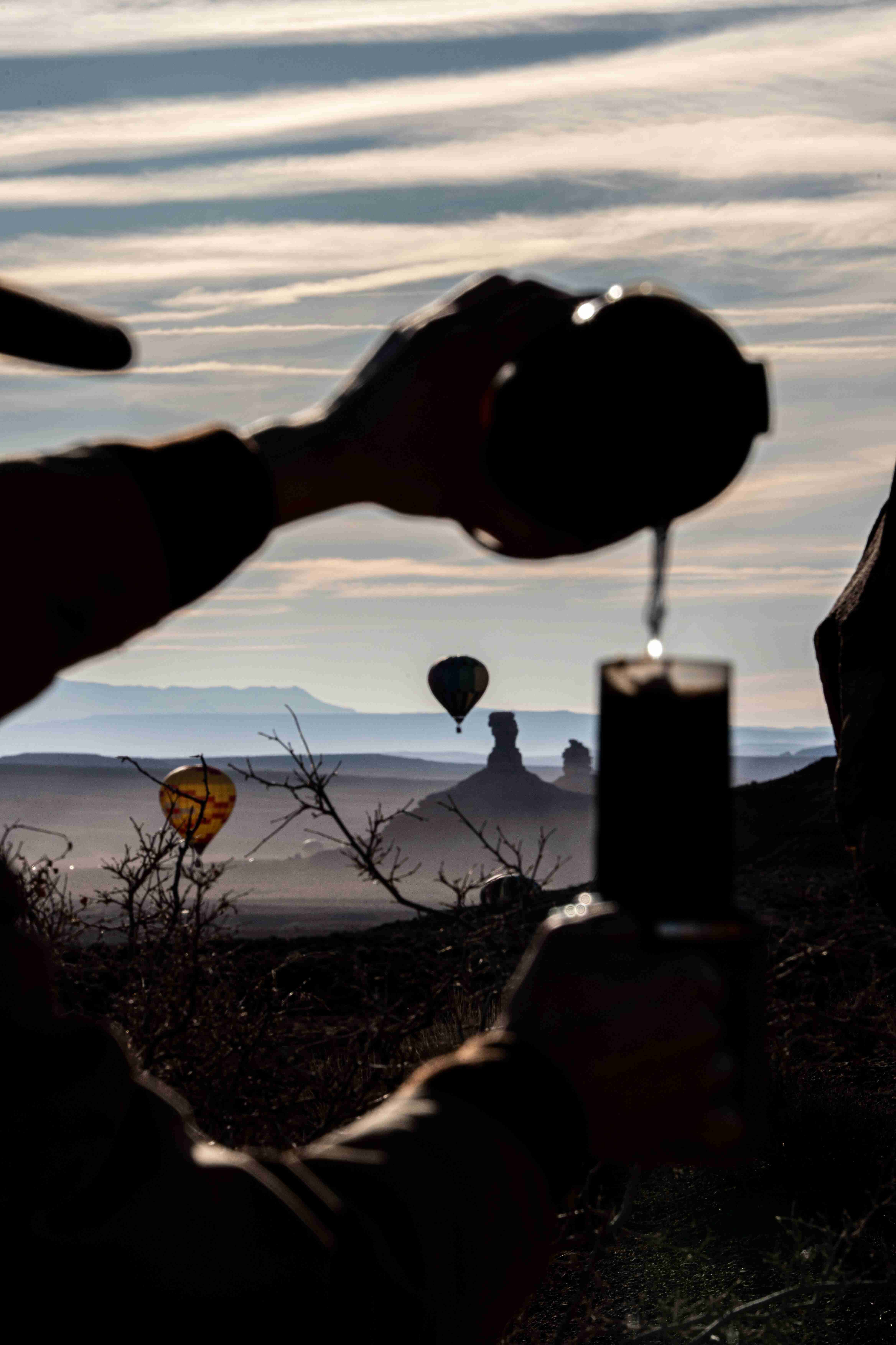 Silhouette of a hand pouring coffee into a cup over the misty valley as balloons rise in the distance