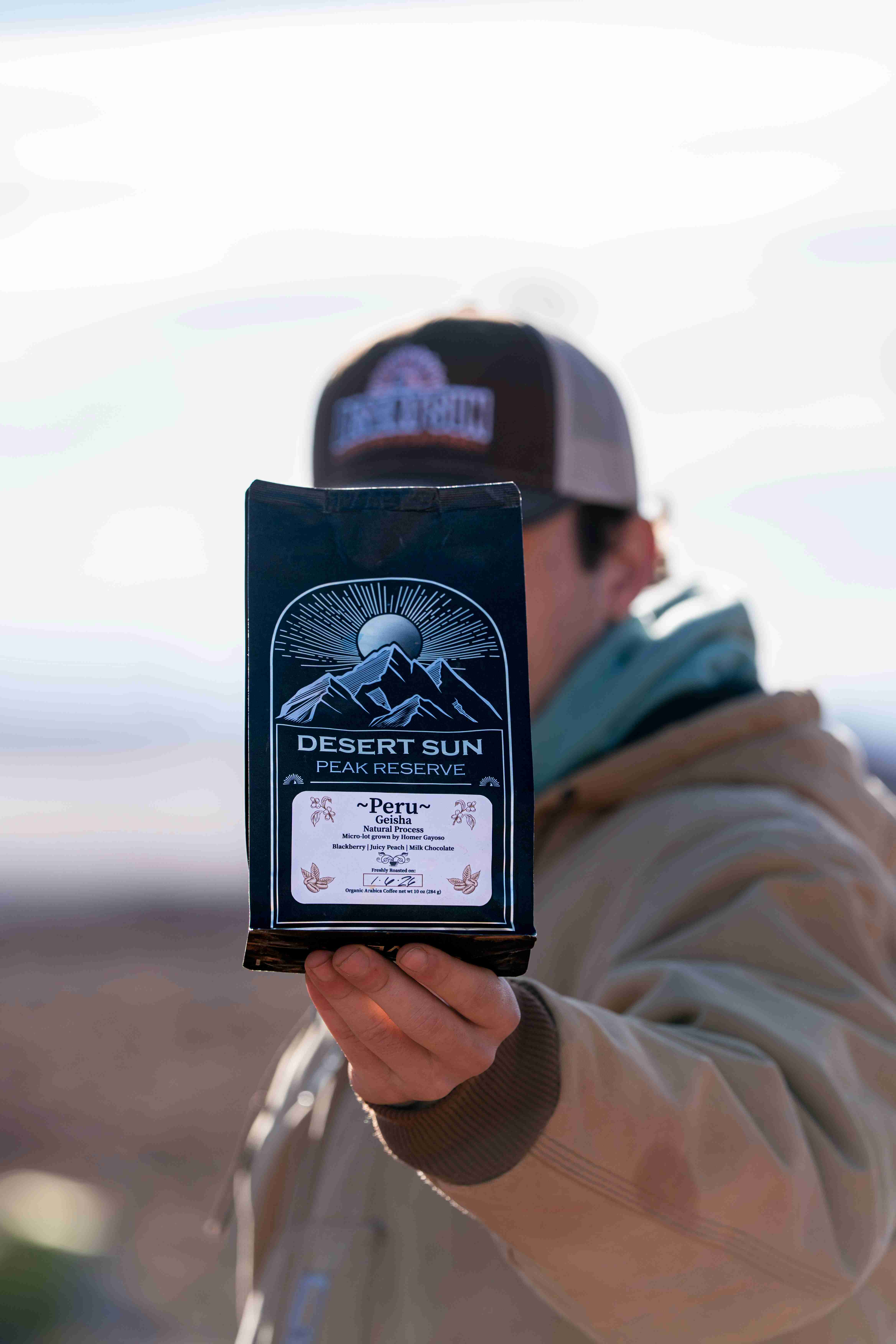 A black bag of Desert Sun Peak Reserve held out toward the camera, its owner's cap blurred behind it