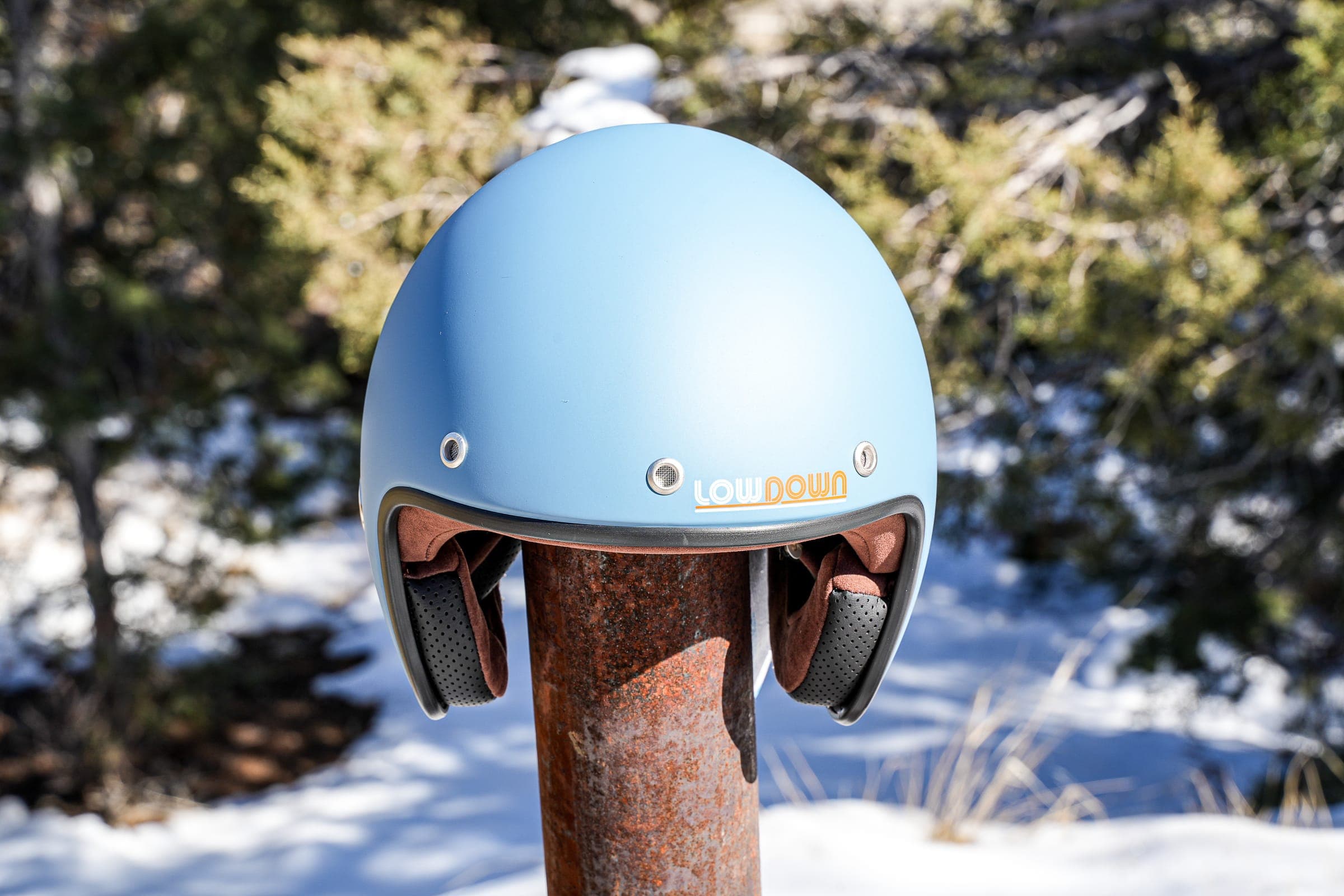 A powder-blue Lowdown helmet resting on a wooden post in the snow among pines