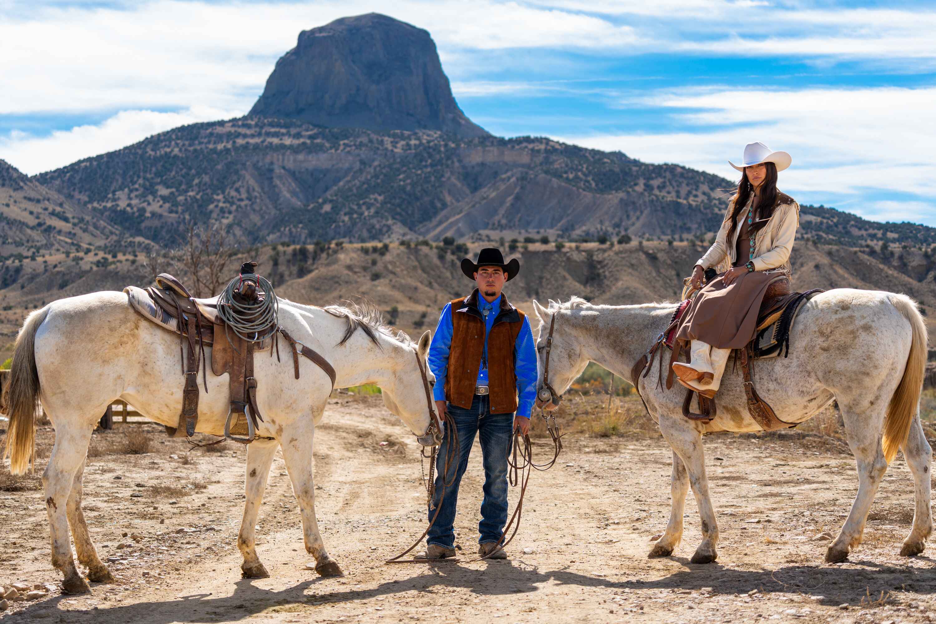 Two riders in western wear with white horses in front of Cabezon Peak — Pinto Ranch content intensive