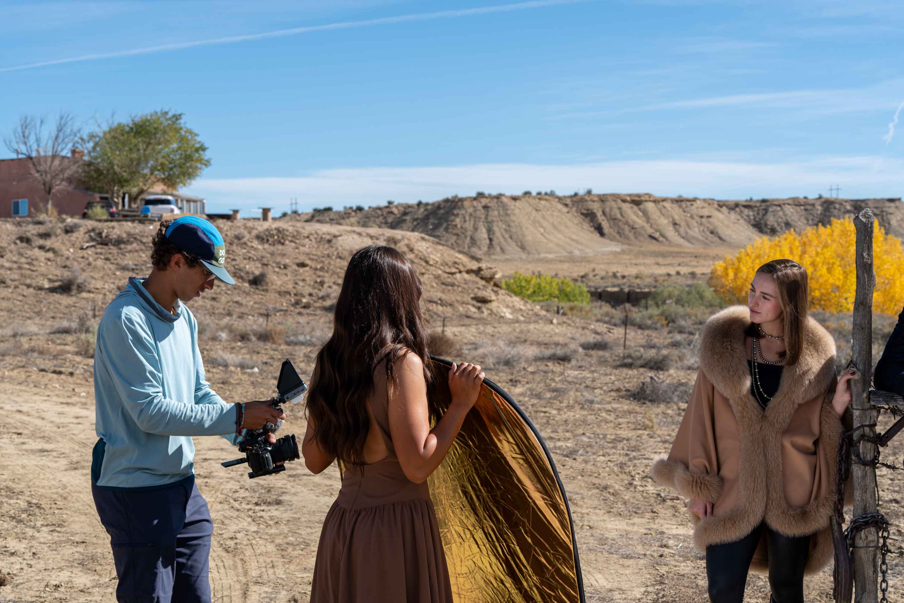 Behind the scenes on the Pinto Ranch content day: a camera operator, a gold reflector, and a model in a fur coat in the New Mexico high desert — a Creative Flow Studio frame.