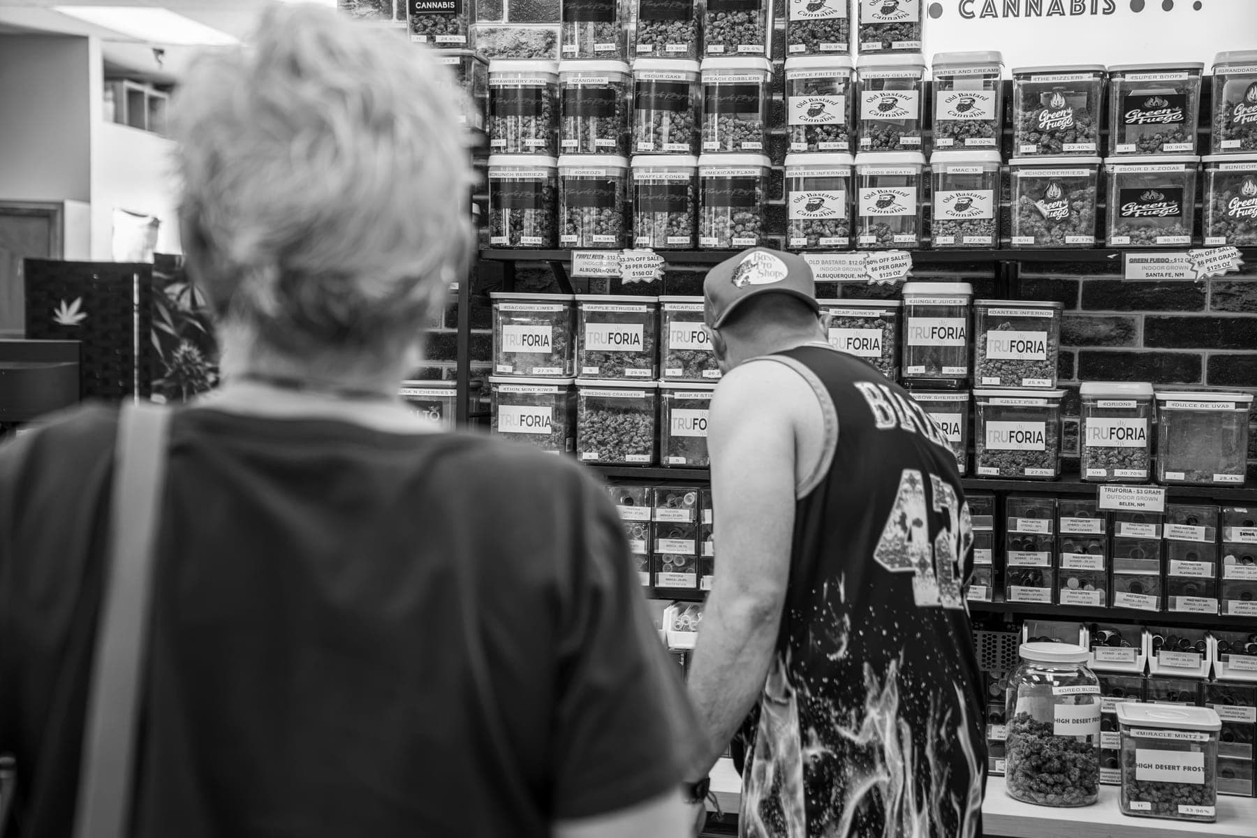 Black-and-white photo of a customer browsing the shop's wall of jars with one of the owners