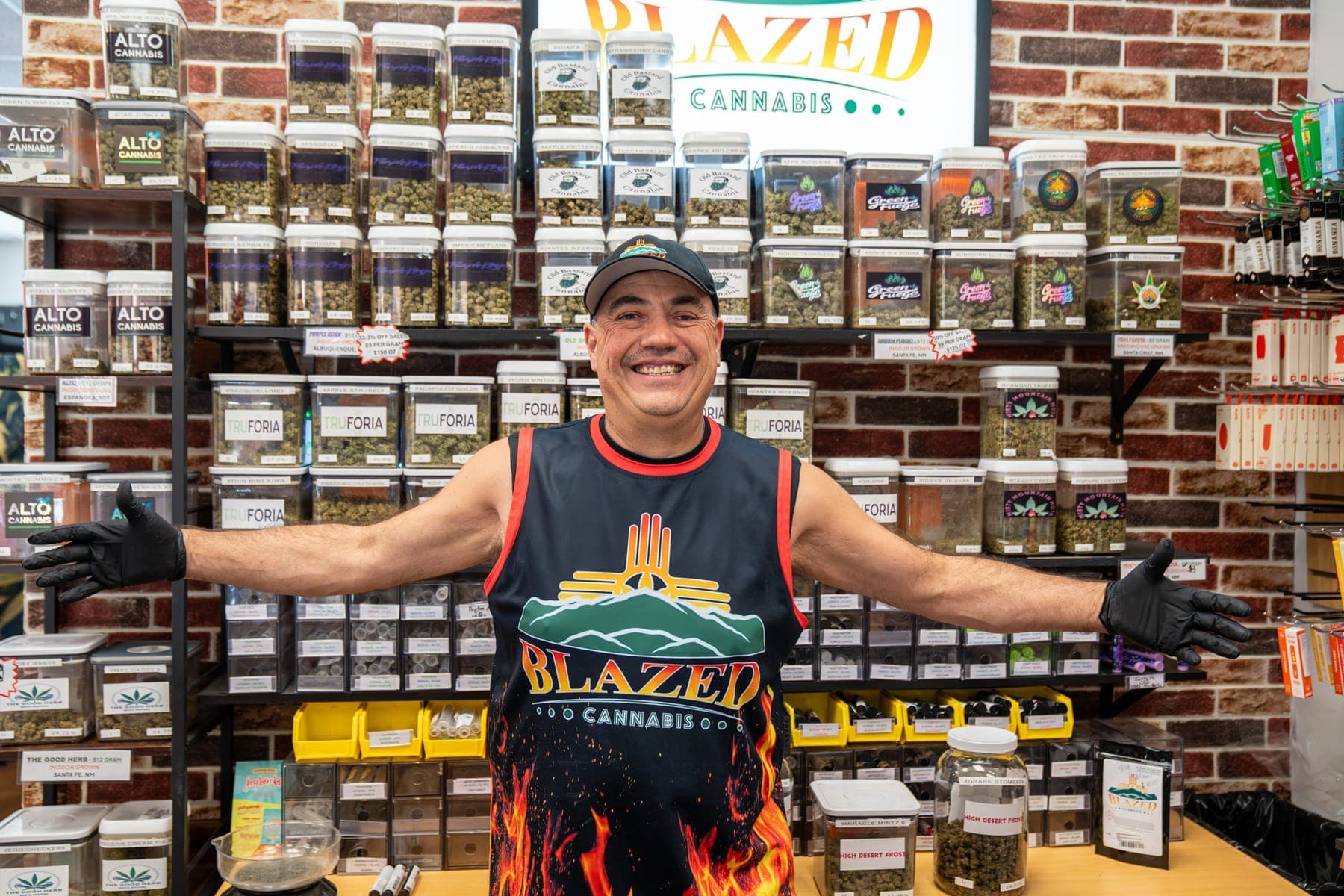 James, one of the owners, with his arms spread wide in front of the shop's brick wall