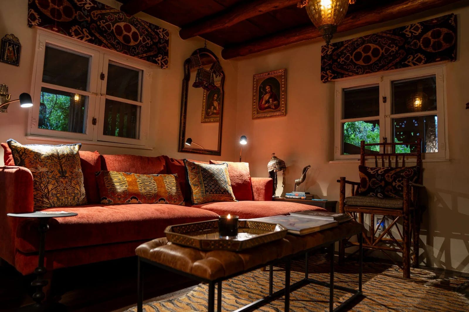 The sitting room at Los Santos: a long red sofa with embroidered pillows, a carved chair, lanterns, and dark vigas overhead