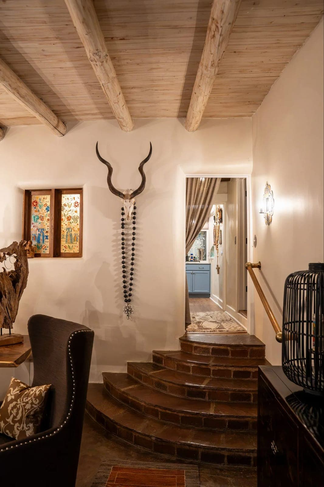 Brick steps leading down into the great room at Los Santos, with a pair of horns and beads on the white plaster wall