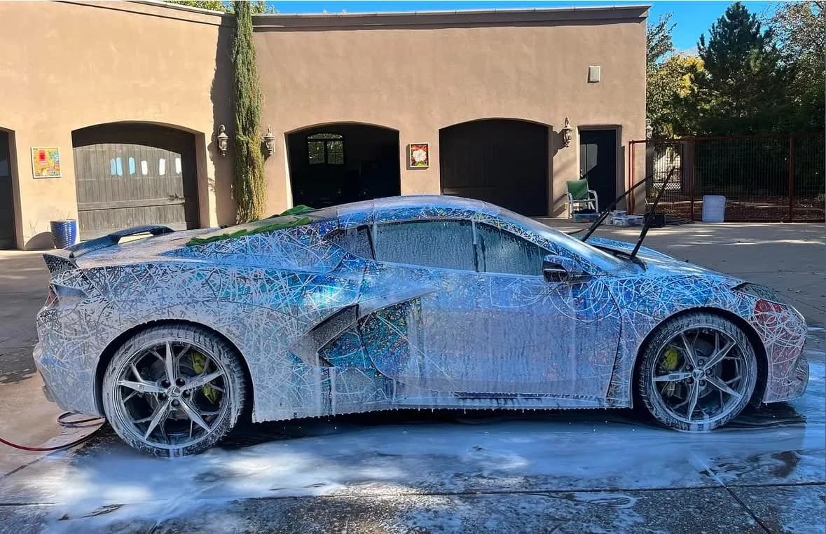 A Corvette covered in wash foam in a sunny driveway in front of arched garage doors, photographed by Cooper Hill