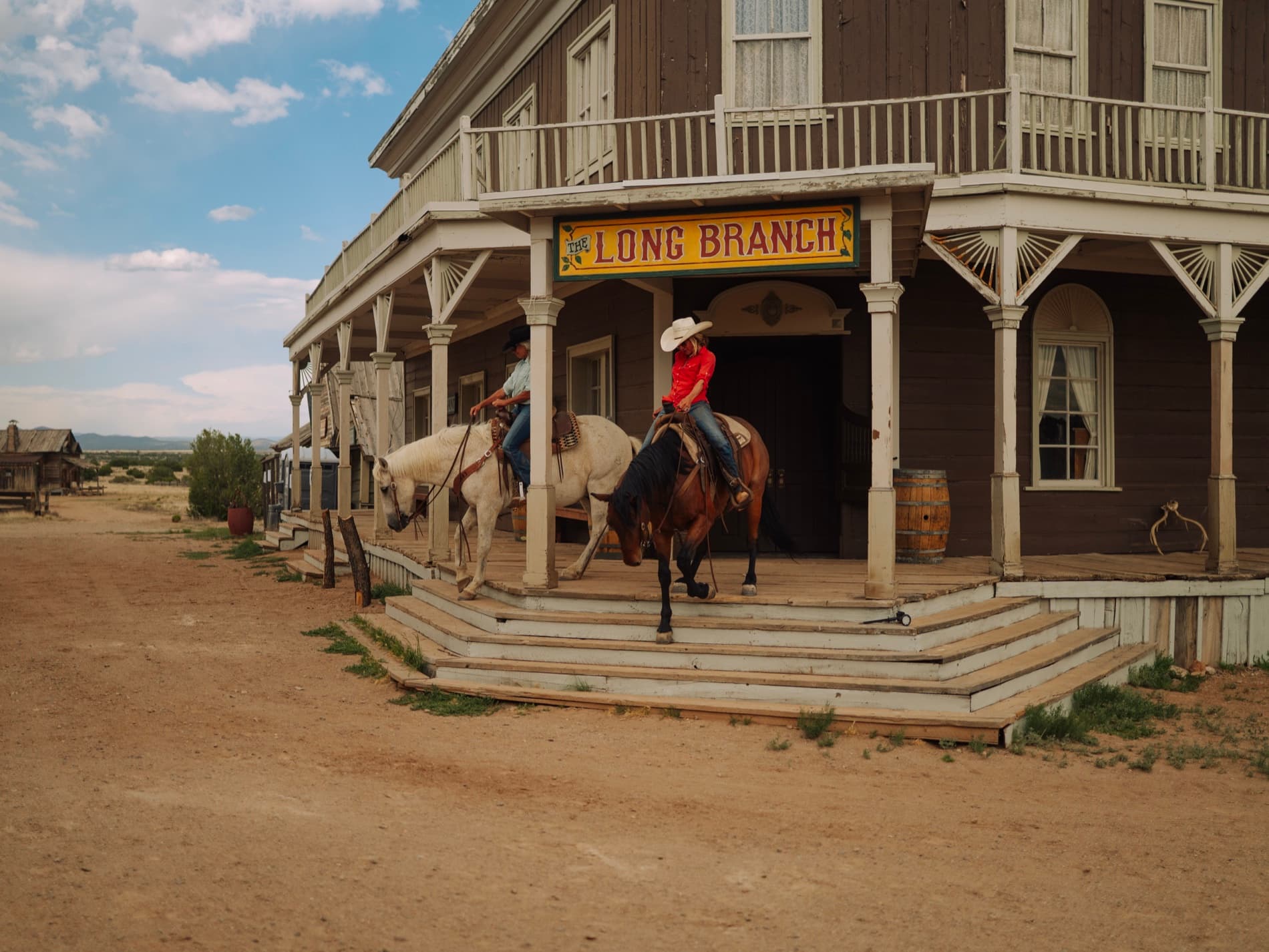 Two riders descending the steps of the Long Branch saloon on the ranch's ghost-town street