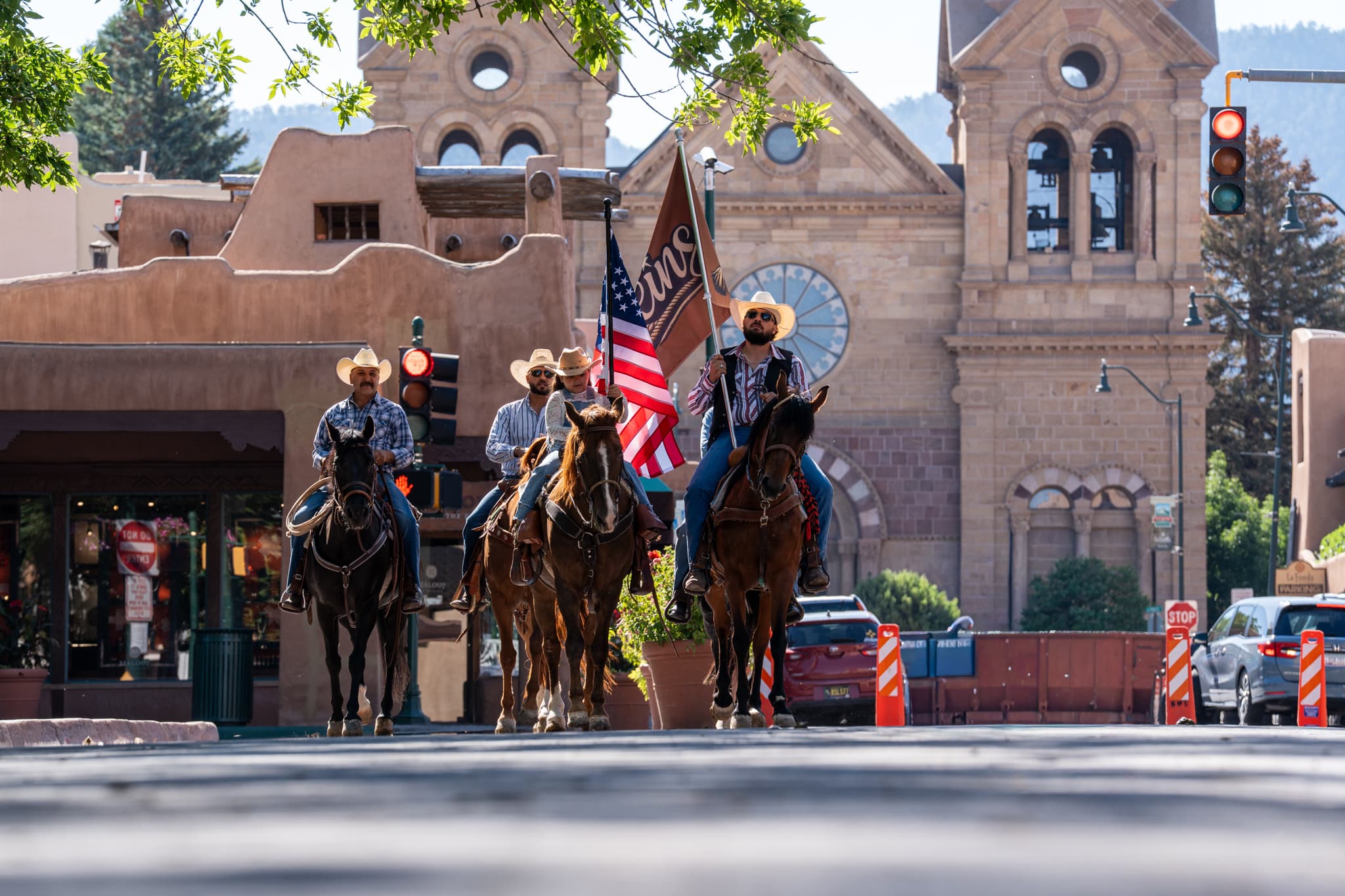 Reins Western Goods riders carrying the brand flag and the American flag toward the camera on the Santa Fe Plaza