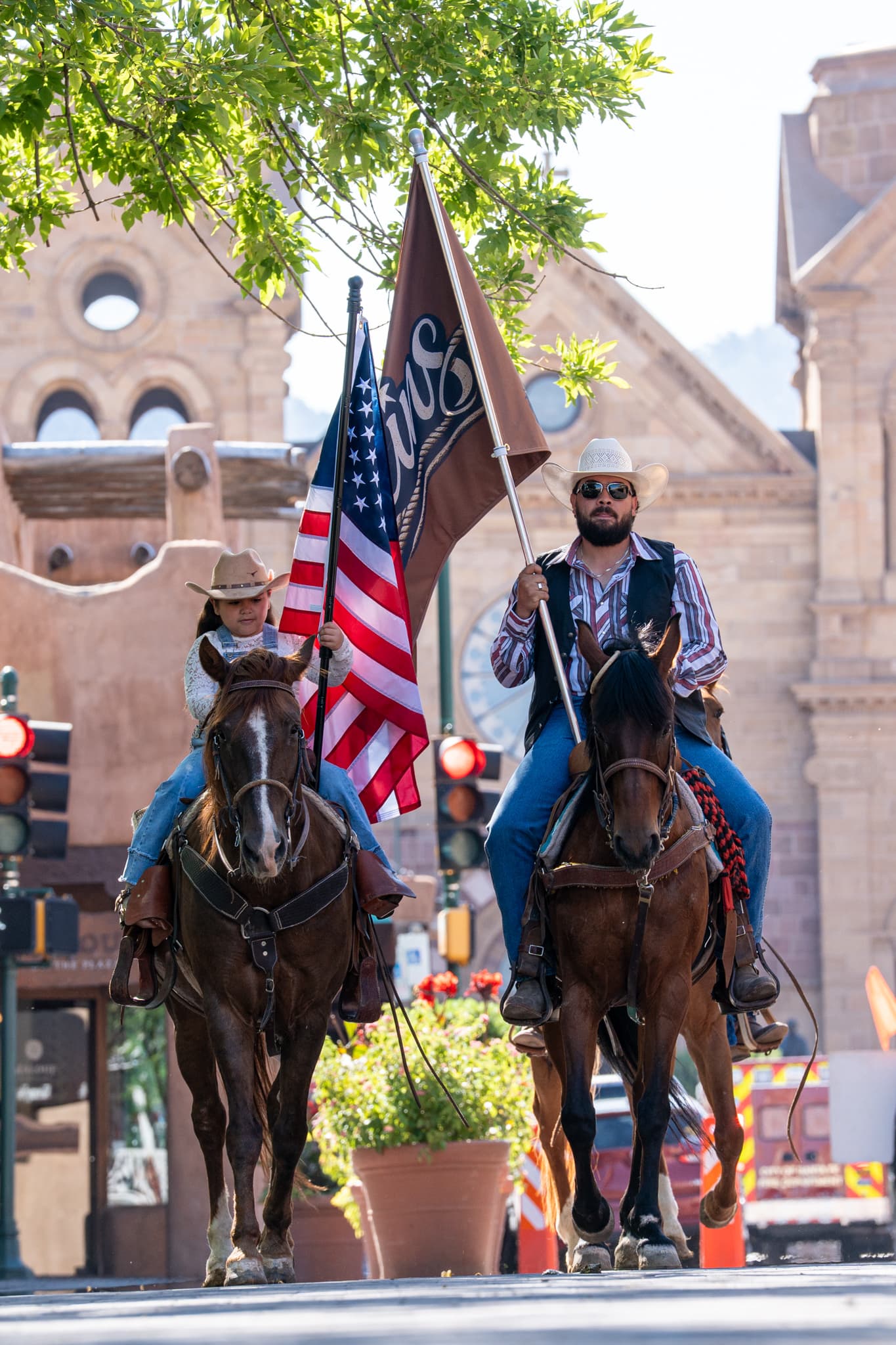 Two riders, one carrying the American flag and one the Reins flag, in front of the cathedral