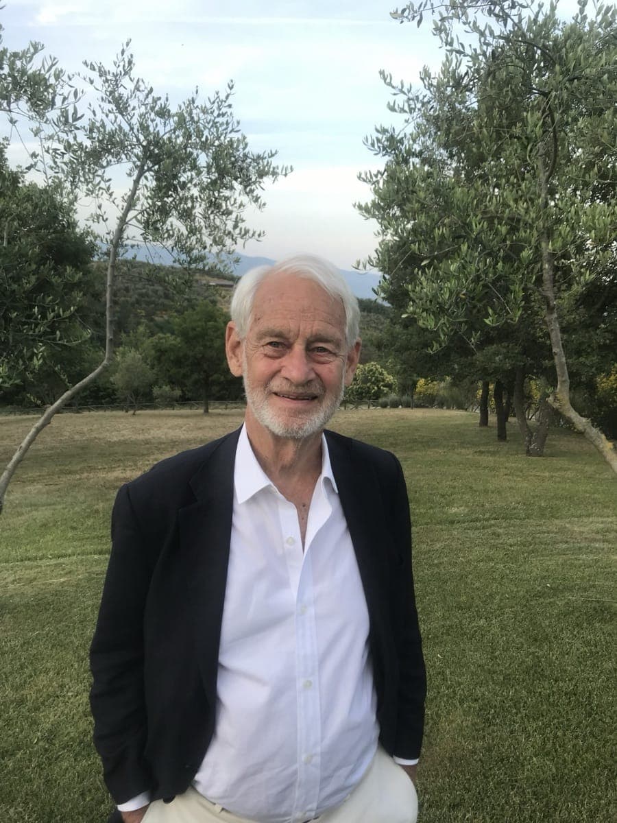 William R. Robins outdoors in a dark jacket, standing in front of green trees